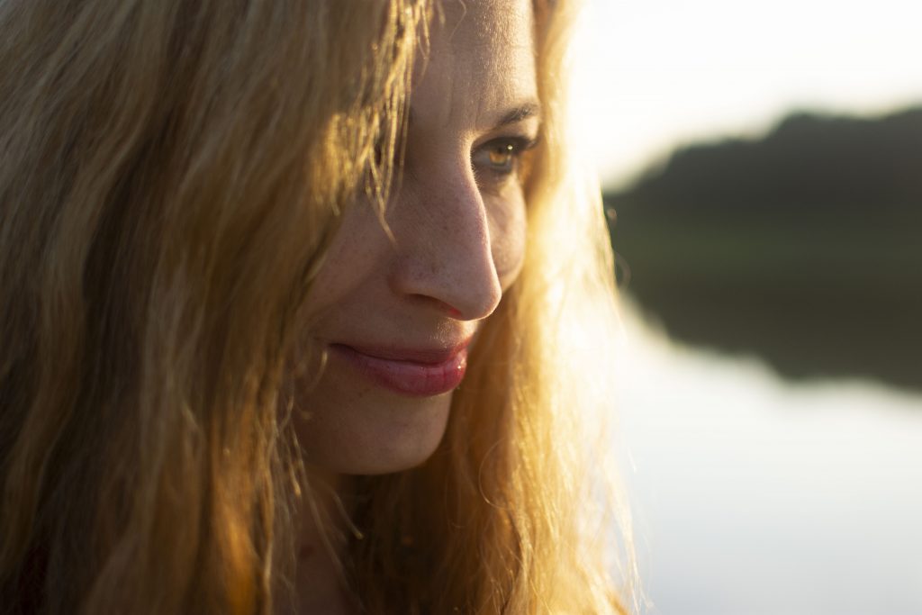 Caroline Wunderlich schaut offen und voller Glück. Hinter ihr liegt ein verschwommener See. Caroline Wunderlich stellt sich vor und freut sich auf Ihre Mails.