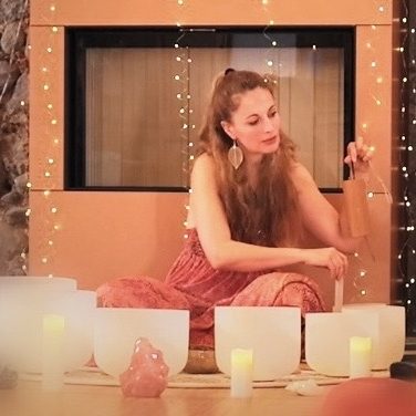 Caroline Wunderlich singt eine Klangmeditation auf dem Innerwise Hof. Sie sitzt hinter ihren Crystal Singing Bowls und hält ein windchime in der Hand.